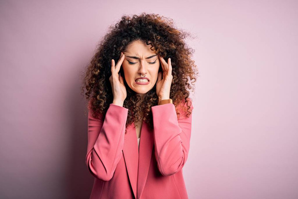 Young beautiful businesswoman with curly hair and piercing wearing elegant jacket with hand on headache because stress. Suffering migraine. - Foto, Bild