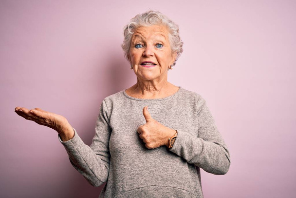Старша красива жінка в повсякденній футболці, що стоїть над ізольованим рожевим тлом, показує руку долоні і робить нормальний жест з великими пальцями вгору, посміхаючись щасливим і веселим
 - Фото, зображення