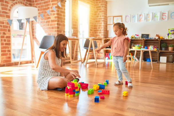 Bela professora e loira criança torre de construção menina usando blocos de plástico no jardim de infância
 - Foto, Imagem