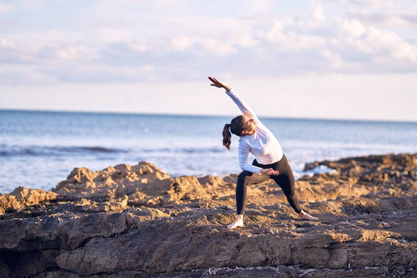 Jeune belle sportive pratiquant le yoga. Coach enseignant la posture guerrière à la plage
 - Photo, image