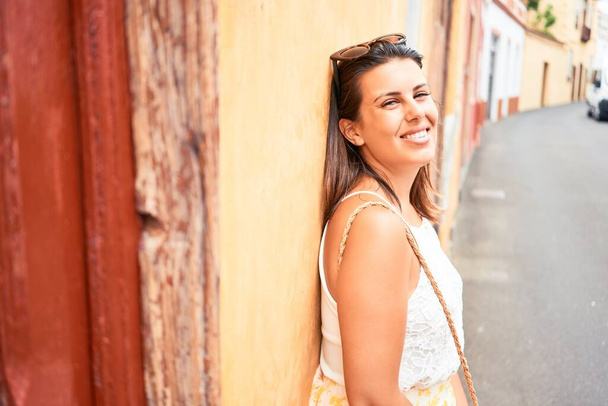 Beautiful girl leaning on orange wall, young friendly woman smiling happy on a sunny day of summer - Foto, Imagen