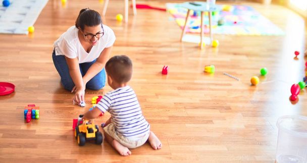 Beautiful teacher and toddler boy playing with tractor and cars at kindergarten - Fotoğraf, Görsel