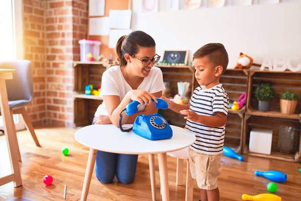 Красивая учительница и малыш играют с винтажным синим телефоном в детском саду
 - Фото, изображение