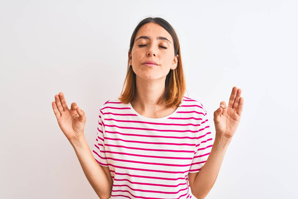 Beautiful redhead woman wearing casual striped pink t-shirt over isolated background relax and smiling with eyes closed doing meditation gesture with fingers. Yoga concept. - Photo, Image