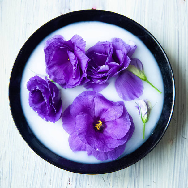 belles fleurs d'eustomes violettes artificielles dans une assiette noire avec du lait sur fond en bois - Photo, image