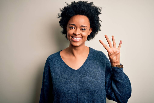 Fiatal gyönyörű afro nő göndör haj visel alkalmi pulóver mutatja, és rámutatva ujjak száma négy, miközben mosolyogva magabiztos és boldog. - Fotó, kép