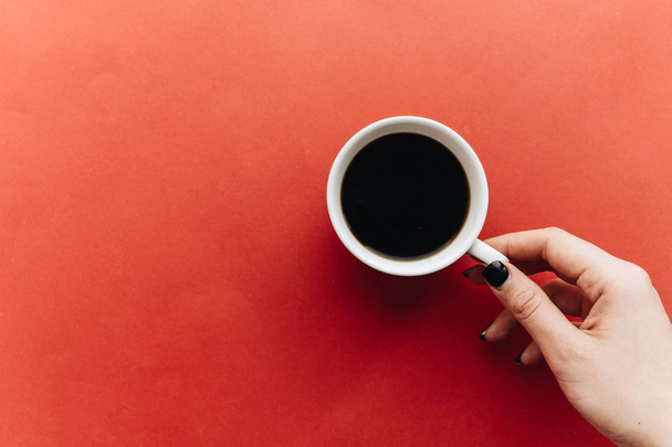 mano femenina sosteniendo taza de café sobre fondo rojo
  - Foto, Imagen