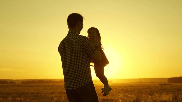 父は腕の中で最愛の子供が飛行中に踊り笑います。幸せな赤ん坊は日没時に父親と遊ぶ。男と子供のシルエット。家族の概念 - 写真・画像