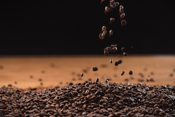 roasted coffee beans falling on pile on black background - 写真・画像