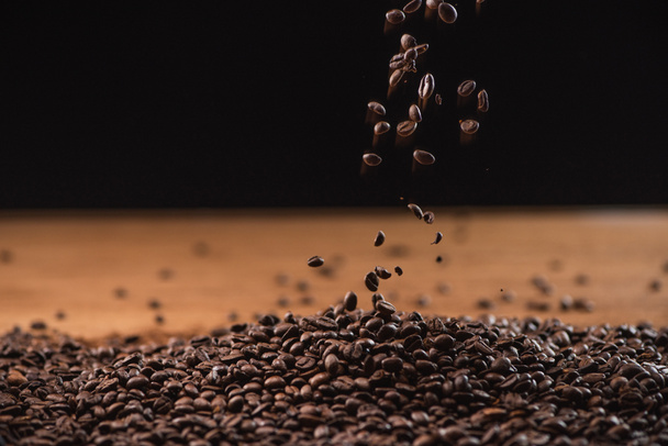 fresh roasted coffee beans falling on pile on black background - Zdjęcie, obraz