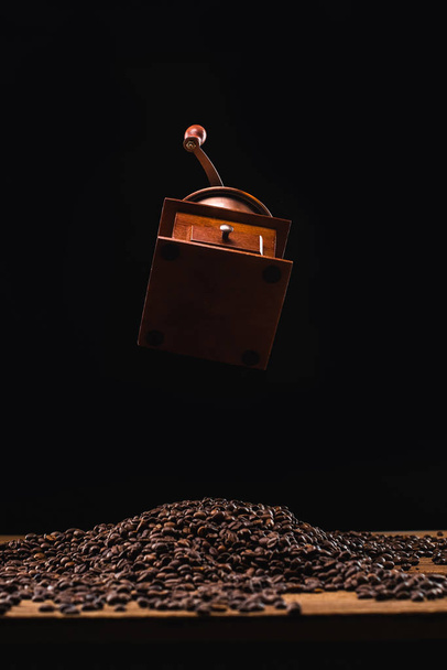 coffee grinder above fresh roasted coffee beans isolated on black - Φωτογραφία, εικόνα