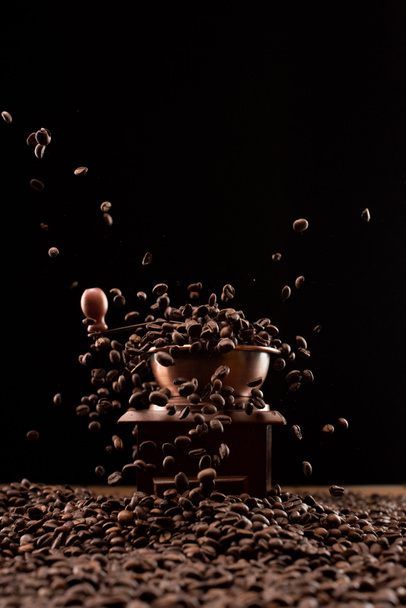 コーヒーグラインダーと黒で隔離された空気中の新鮮な焙煎コーヒー豆 - 写真・画像