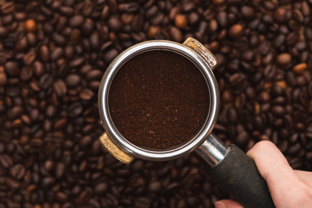 cropped view of woman holding ground coffee in filter holder above fresh roasted coffee beans - Foto, immagini