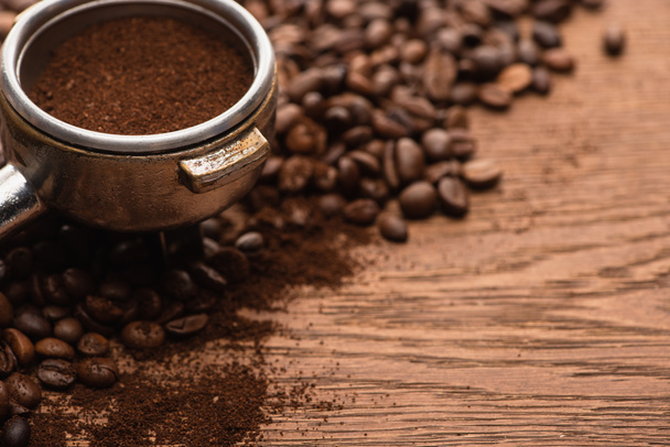Nahaufnahme von frisch gerösteten Kaffeebohnen und gemahlenem Kaffee in Filterhalter auf Holztisch - Foto, Bild