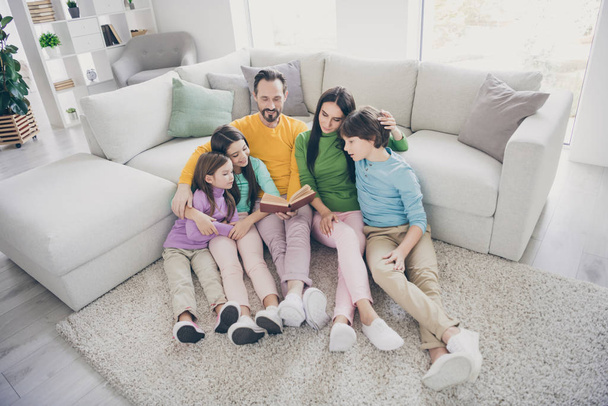 Top above high angle view photo of positive cheerful fun family sit floor carpet near sofa couch dad read book mom three preteen little adopted kids listen story enjoy novel in room house - Фото, зображення