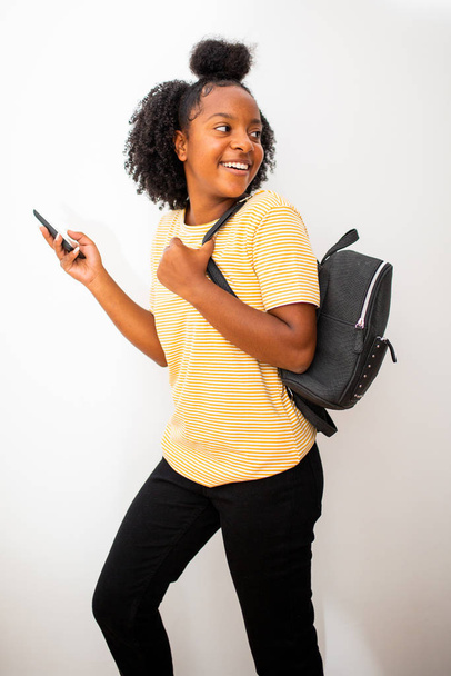 Perfil retrato de niña afroamericana sonriente con bolsa y teléfono móvil girando fondo blanco aislado
 - Foto, imagen