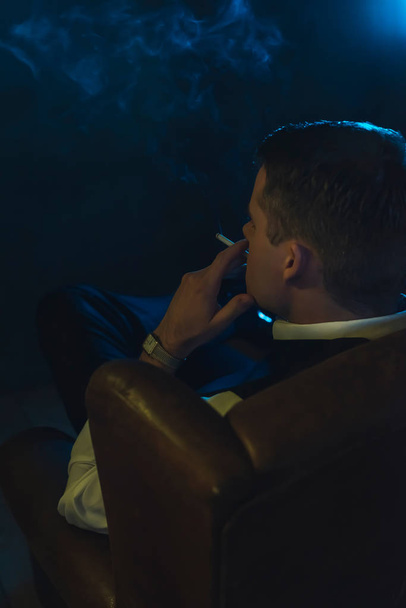 Ретро мода человек курит сигарету и сидит в коже
 - Фото, изображение