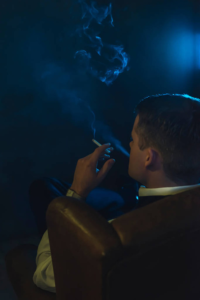 Retro fashion man smokes a cigarette and is sitting in leather a - Фото, зображення