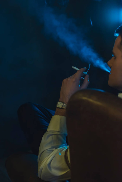 Retro άνθρωπος της μόδας καπνίζει ένα τσιγάρο και κάθεται σε δέρμα ένα - Φωτογραφία, εικόνα