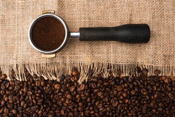 vrchní pohled na čerstvě pražená kávová zrna a pytlovinu s držákem na filtry s mletou kávou - Fotografie, Obrázek
