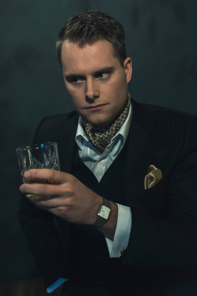 Retro fashion man in dark suit holds a glass of whiskey. - 写真・画像