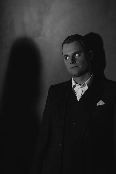 Retro mode man in donker pak met boze blik staat tegen wa - Foto, afbeelding