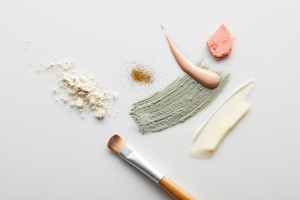 Top view of face powder, clay, cosmetic and tone cream brushstrokes, brush, blusher and golden sparkles on grey background - Foto, Imagen