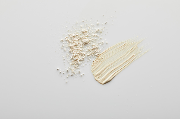 Top view of tone cream brushstrokes and face powder on grey background - Foto, Imagem