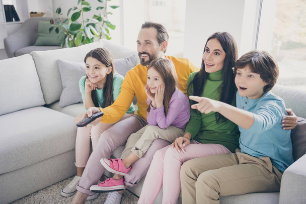 Dream harmony family spending time concept. Five people dad daddy mom mommy three kids boy girls sit divan watch tv schoolboy point index finger hold remote control in room living room - Valokuva, kuva