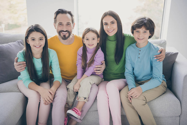 Positive loving cheerful ideal family concept. Mom daddy sit couch hug embrace her three children schoolboy schoolgirl in house living room - 写真・画像