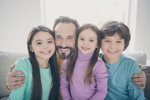 Portrait of positive cheerful loving family dad daddy hug his cute lovely kids two girls boy son younger sister sit divan in house indoors - Photo, Image