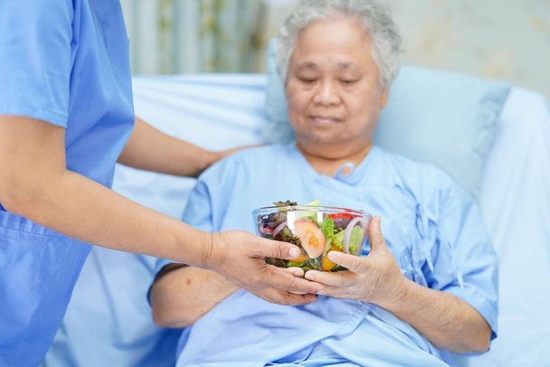 Lekarz dać sałatki warzywa śniadanie zdrowe jedzenie do azjatyckiego seniora lub starszej pani pacjenta z nadzieją i szczęśliwy podczas siedzenia i głodny w łóżku w szpitalu. - Zdjęcie, obraz