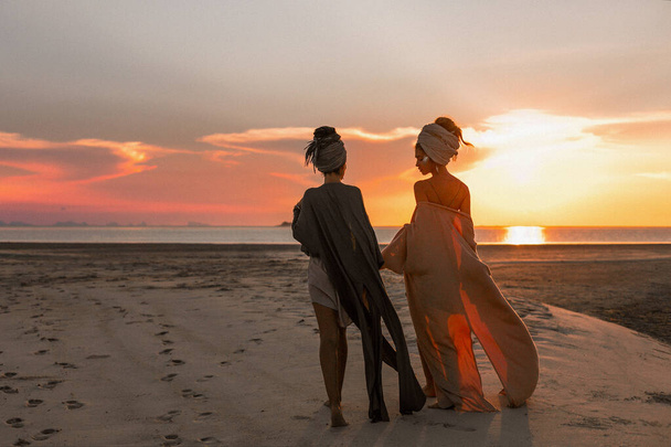 dos chicas hermosas jóvenes en turbante en la playa al atardecer
  - Foto, imagen