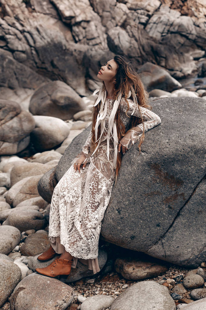 stylish young bohemian woman posing on stone beach background - 写真・画像