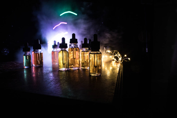 Vape concept. Smoke clouds and vape liquid bottles on dark background. Light effects. Useful as background or vape advertisement or vape background. Selective focus - Photo, Image