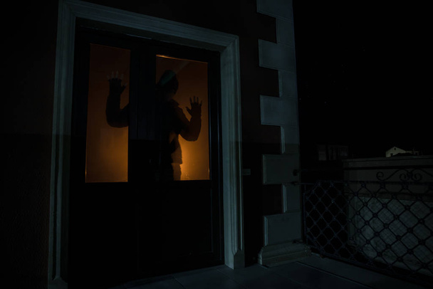 Silhouette of an unknown shadow figure on a door through a closed glass door. The silhouette of a human in front of a window at night. Scary scene halloween concept of blurred silhouette of maniac. - Foto, Imagen