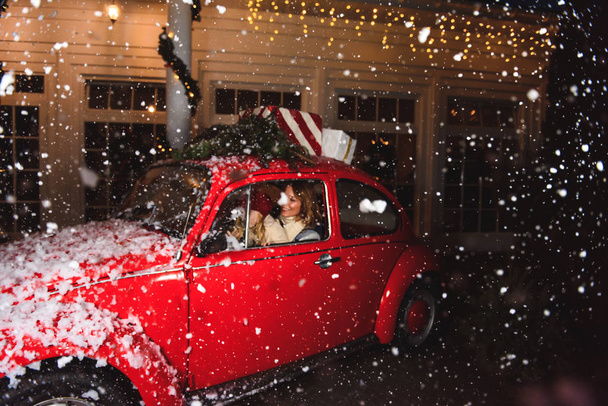 Christmas. Mom with daughter laughing in a red car under the snow - Fotó, kép