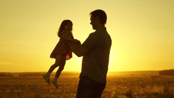 Ο μπαμπάς αγαπημένο παιδί στην αγκαλιά της χορεύει στην πτήση και γελάει. Το χαρούμενο μωρό παίζει με τον πατέρα του το ηλιοβασίλεμα. Η σιλουέτα ενός άντρα και ενός παιδιού. Οικογενειακή έννοια - Φωτογραφία, εικόνα