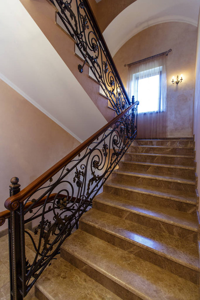 Stairs in the cottage with wrought iron railings and wooden handrails. Marble steps. - Photo, Image