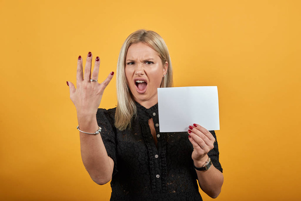 Раздражённая женщина держит в руке пустой лист бумаги и демострирующие пальцы.
 - Фото, изображение