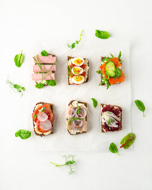Válogatás dán smorrebrod nyitott szendvicsek, zöld saláta levelek pergamen papír fehér alapon - Fotó, kép