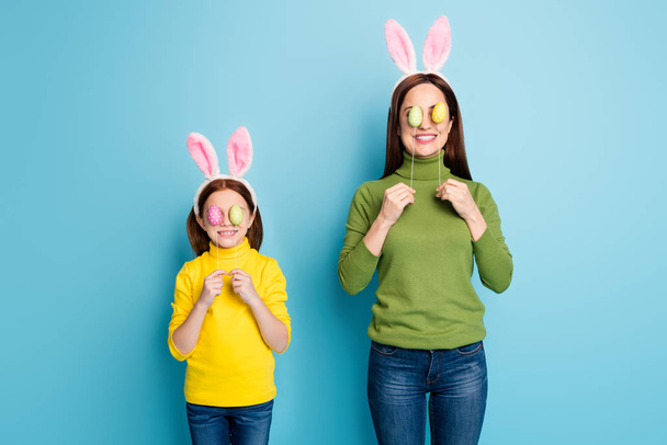 Portrait of nice attractive lovely childish playful cheerful cheery girls covering eyes with eggs sticks having fun isolated over bright vivid shine vibrant blue color background - Фото, зображення