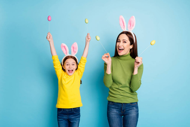 Portrait of nice attractive lovely glad cheerful cheery girls mom mum holding in hands eggs sticks having fun isolated over bright vivid shine vibrant blue color background - Photo, image