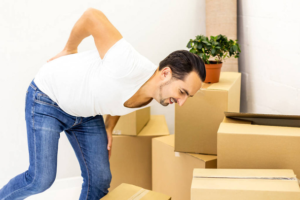 Man suffering from cramp in back while stacking boxes, preparing for relocation. - 写真・画像
