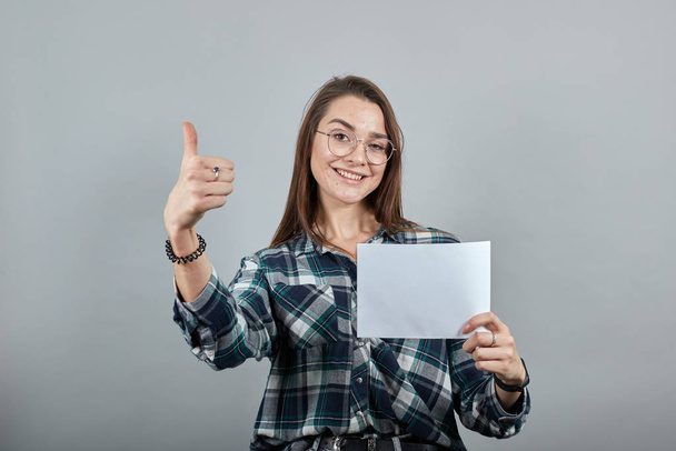 mulher feliz com óculos segura uma folha branca de papel na mão, mostra seu polegar
 - Foto, Imagem