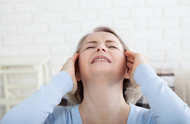 Woman suffering from stress or a headache grimacing in pain as she holds the back of her neck with her other hand to her temple, with copyspace. Concept photo with indicating location of pain. - Fotografie, Obrázek