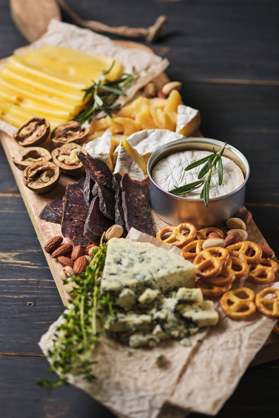 Delicious snacks. Several varieties of cheese, pretzels, nuts and sausage on an old wooden table. Food for a romantic dinner. - Photo, Image