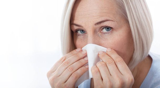 Healthcare, cold, allergy and people concept, sick woman blowing her runny nose in paper tissue on white background - Foto, afbeelding