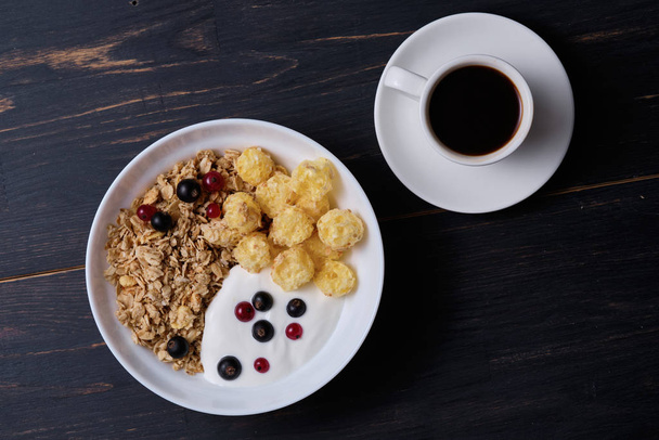 Müsli mit Joghurt und frischen Beeren im Teller. Frühstück auf einem dunklen Holztisch. - Foto, Bild