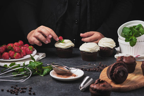 カップケーキを作るプロセス。フレーム内の料理人の手.クリーム、新鮮なベリー、チョコレート、ミントとデザート。チョコレートガナッシュのぬいぐるみ. - 写真・画像